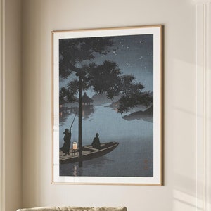 May include: A framed print of a Japanese woodblock print depicting a boat with two figures on a lake at night. The scene is illuminated by a lantern and the stars in the sky. The print is in a light wood frame and is hanging on a wall.