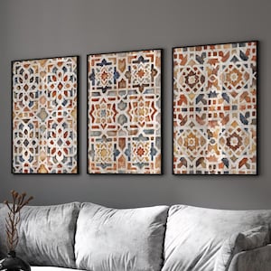 Puede incluir: Tres obras de arte murales enmarcadas con patrones geométricos en tonos de rojo, naranja, azul y blanco. La obra de arte se exhibe sobre un sofá gris en un salón moderno. Los marcos son negros.