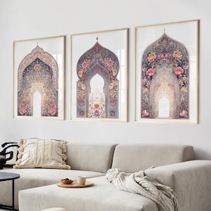 Puede incluir: Tres impresiones artísticas enmarcadas con diseños de arcos ornamentados con patrones florales en tonos rosa, azul y dorado. Las impresiones se exhiben sobre un sofá seccional beige en un salón.