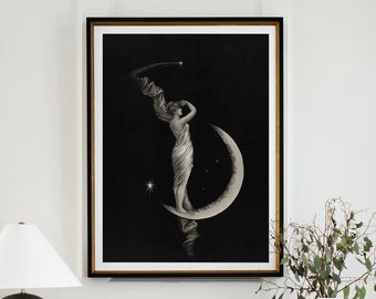 May include: A black and white illustration of a woman standing on a crescent moon with stars in the background. The illustration is framed and hanging on a white wall above a black metal console table with books and a lamp.