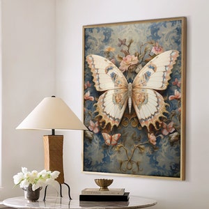 以下が含まれることがあります： 青と金の色の花柄の背景に、複雑な模様の白と金の蝶が描かれた額装されたプリント。プリントは白い壁にかけられており、その下には大理石のテーブルと白いオットマンが2つ置かれている。