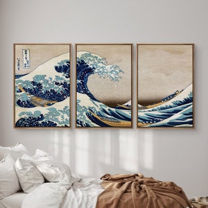 Puede incluir: Un conjunto de tres impresiones enmarcadas que representan una impresión japonesa tradicional en madera de una gran ola rompiendo sobre un barco. La ola es azul y blanca, y el barco es amarillo y marrón. Las impresiones están enmarcadas en un marco de madera simple.