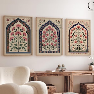 May include: Three framed prints featuring a floral design in a traditional Indian style. The prints depict a central floral motif with intricate details and a cream background. The frames are a light wood colour.