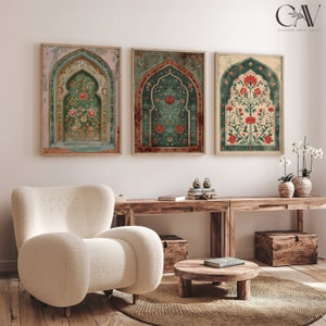 May include: Three framed prints depicting intricate floral designs in shades of green, red, and cream. The prints feature arched doorways with ornate details and are displayed against a white wall. The prints are positioned above a wooden table with a white armchair and a small wooden table.