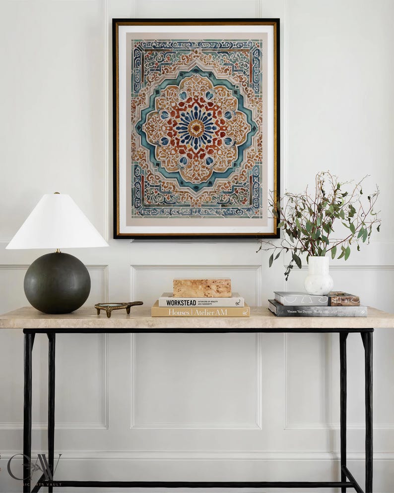K&ouml;nnte beinhalten: Ein gerahmter Druck mit einem aufwendigen, symmetrischen Design in Blau-, Rot- und Beiget&ouml;nen h&auml;ngt &uuml;ber einer Konsole. Der Tisch hat eine Marmorplatte, schwarze Metallbeine und ist mit B&uuml;chern, einer Lampe und einem kleinen dekorativen Objekt ausgestattet.