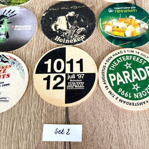Pu&ograve; includere: Una collezione di sottobicchieri circolari in cartone con vari design grafici, tra cui il marchio Heineken, pubblicit&agrave; di festival jazz con date come 1997 e 2000 e un logo Theaterfeest Parade. Una piccola etichetta bianca riporta la scritta Set 2.
