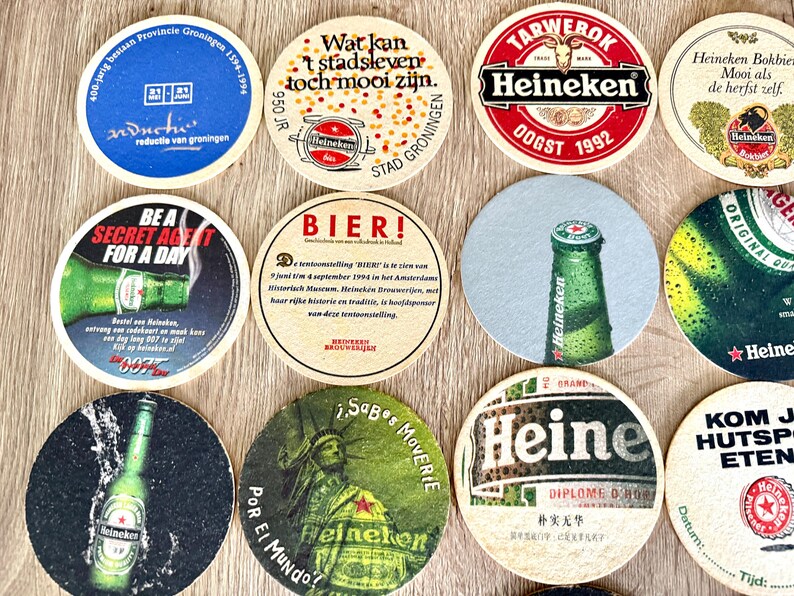 Pu&ograve; includere: Una collezione di dodici sottobicchieri circolari in cartone con vari marchi Heineken, grafiche promozionali e testo tra cui 'Be a Secret Agent for a Day', 'Bier!' e 'Heineken Bokbier'. I sottobicchieri mostrano colori, loghi e immagini diversi.