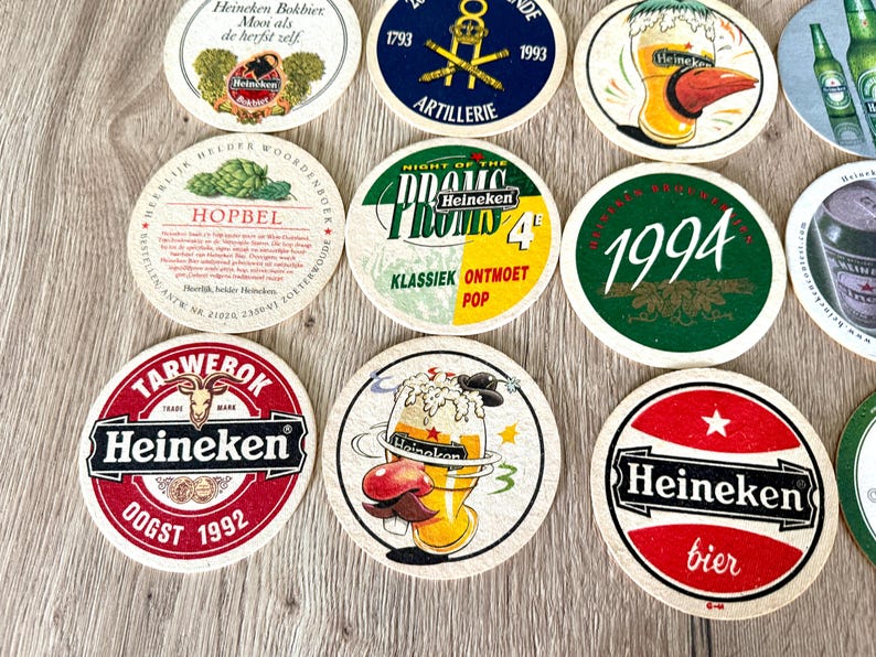 Pu&ograve; includere: Una collezione di sottobicchieri rotondi in cartone con vari marchi Heineken, inclusi loghi, date come 1992 e 1994, e illustrazioni grafiche di bicchieri di birra, luppolo e testi come Night of the Proms e Hopbel.