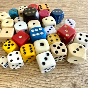 May include: A large collection of assorted six-sided dice in various colors including white, red, blue, yellow, black, and wood tones. The dice feature black or white pips representing numbers one through six, with varying sizes and finishes scattered.
