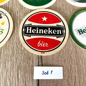 Pu&ograve; includere: Una collezione di sottobicchieri circolari in cartone con vari design del marchio Heineken. Il sottobicchiere centrale mostra una grafica rossa e bianca con il testo Heineken bier e una piccola stella. Un'etichetta bianca rettangolare riporta Set 1.