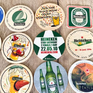 Pu&ograve; includere: Una collezione di undici sottobicchieri in cartone circolari e quadrati con vari marchi Heineken, inclusi grafiche di bicchieri da birra, bottiglie, barche a vela e testi di eventi come Star Saturday 22.05.10 e Whitbread Round the World Race.