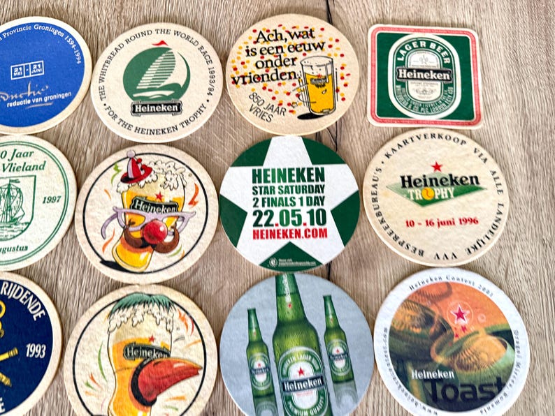 Pu&ograve; includere: Una collezione di undici sottobicchieri in cartone circolari e quadrati con vari marchi Heineken, inclusi grafiche di bicchieri da birra, bottiglie, barche a vela e testi di eventi come Star Saturday 22.05.10 e Whitbread Round the World Race.