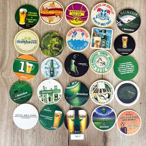 Pu&ograve; includere: Una collezione di venticinque sottobicchieri in cartone, di forma circolare e quadrata, con vari disegni grafici, loghi di marchi e testi in diverse lingue, disposti a griglia su una superficie in legno di colore chiaro.