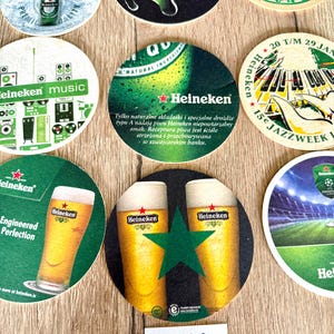 Pu&ograve; includere: Una collezione di sottobicchieri rotondi in cartone con vari marchi Heineken, inclusi grafiche di bottiglie di birra, bicchieri, attrezzature musicali e temi jazz, con testo in diverse lingue e una piccola etichetta bianca con scritto Set 3.
