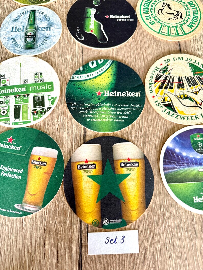 Pu&ograve; includere: Una collezione di sottobicchieri rotondi in cartone con vari marchi Heineken, inclusi grafiche di bottiglie di birra, bicchieri, attrezzature musicali e temi jazz, con testo in diverse lingue e una piccola etichetta bianca con scritto Set 3.