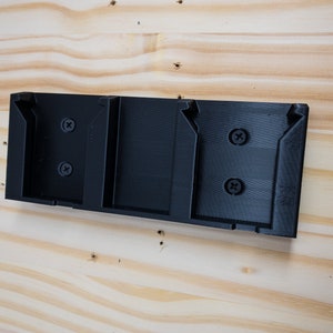 Puede incluir: Un soporte de pared de pl&aacute;stico negro con tres ranuras para sujetar objetos. El soporte tiene dos tornillos a cada lado.