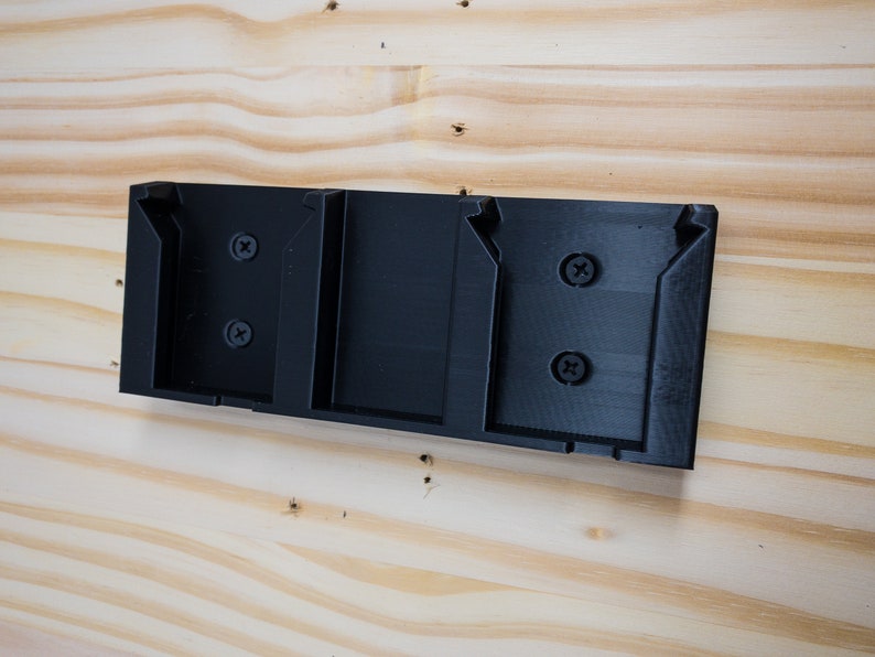Puede incluir: Un soporte de pared de pl&aacute;stico negro con tres ranuras para sujetar objetos. El soporte tiene dos tornillos a cada lado.