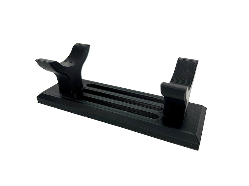 Puede incluir: Soporte de pl&aacute;stico negro con dos brazos curvos para sujetar un sable de luz u otro objeto largo. El soporte tiene tres ranuras para sujetar el objeto en su lugar.