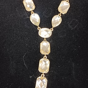 May include: A gold chain necklace with a long, dangling pendant featuring a series of clear, faceted crystals.