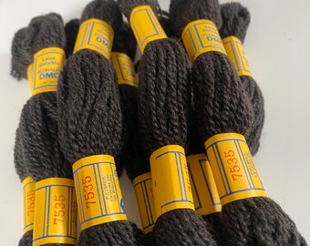 May include: A collection of dark brown yarn skeins with yellow and blue labels. The labels display the number 7535 and the DMC logo. The yarn is tightly wound, and the skeins are arranged in a slightly overlapping pattern.