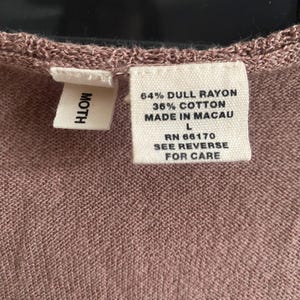 Puede incluir: Primer plano de una etiqueta de prenda de color malva con la marca "MOTH". La etiqueta incluye la composici&oacute;n de la tela: 64% ray&oacute;n opaco, 36% algod&oacute;n, y el texto "MADE IN MACAU". La talla es L, con RN 66170 e instrucciones de cuidado.