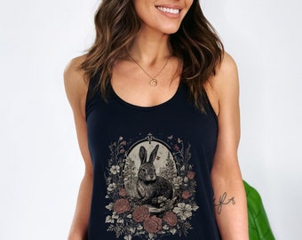 May include: A navy blue vest top with a detailed illustration of a rabbit surrounded by flowers and foliage. The design is framed within an oval shape, with a vintage aesthetic. The artwork is in shades of brown, beige, and cream.