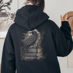May include: Black hooded sweatshirt with a graphic print of a raven perched on a stone structure. The graphic includes the word "NEVERMORE" in a stylized font.