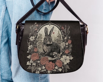 May include: A brown leather shoulder bag featuring a floral and rabbit design. The bag has a flap closure and a long adjustable strap.