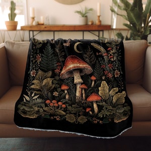 Może przedstawiać: Czarny koc z kolorową ilustracją grzybów i liści. Wzór zawiera półksiężyc i różne rodzaje grzybów w odcieniach czerwieni, pomarańczy i brązu.