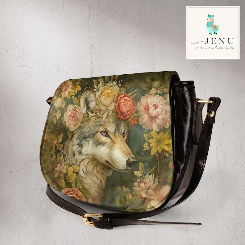 May include: A black leather crossbody bag with a floral print featuring a wolf wearing a flower crown. The bag has a gold buckle and a long adjustable strap.