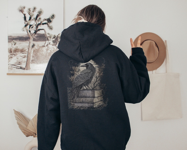 May include: Black hooded sweatshirt with a graphic print of a raven perched on a stone structure. The graphic includes the word "NEVERMORE" in a stylized font.