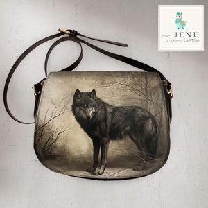 May include: A brown leather crossbody bag featuring a wolf illustration on the front. The wolf is black and white and is standing in a woodland setting. The bag has a gold buckle and a long strap.