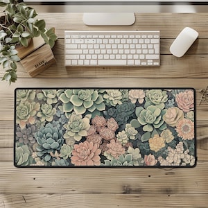 May include: A rectangular desk mat featuring a detailed floral pattern of succulents in shades of green, pink, and yellow. The mat has a black border and is placed on a wooden desk, alongside a keyboard, mouse, and plant.