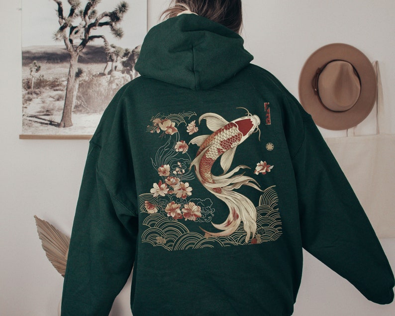 Pu&ograve; includere: Una felpa con cappuccio verde scuro con un grande disegno ricamato di un pesce koi che nuota attraverso un motivo floreale. Il disegno &egrave; in oro, rosso e bianco.