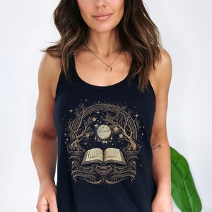 Puede incluir: Una camiseta sin mangas negra con una ilustración dorada de un libro, una luna y árboles. El diseño incluye estrellas y un tema celestial. La camiseta sin mangas es sin mangas y tiene cuello redondo.