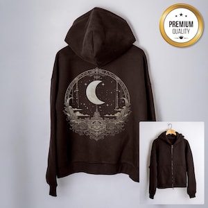Puede incluir: Una sudadera con capucha con cremallera marrón oscuro con un gráfico detallado en la espalda que representa una luna creciente, estrellas y elementos arquitectónicos. La sudadera con capucha tiene una capucha y una cremallera frontal. Un sello de "Premium Quality" es visible.
