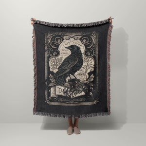 May include: Black and white woven throw blanket with a vintage illustration of a crow perched on a branch. The illustration is surrounded by a decorative frame with the text "Cogito Ergo Sum" and "Difficile est Satyram Non Scribere".