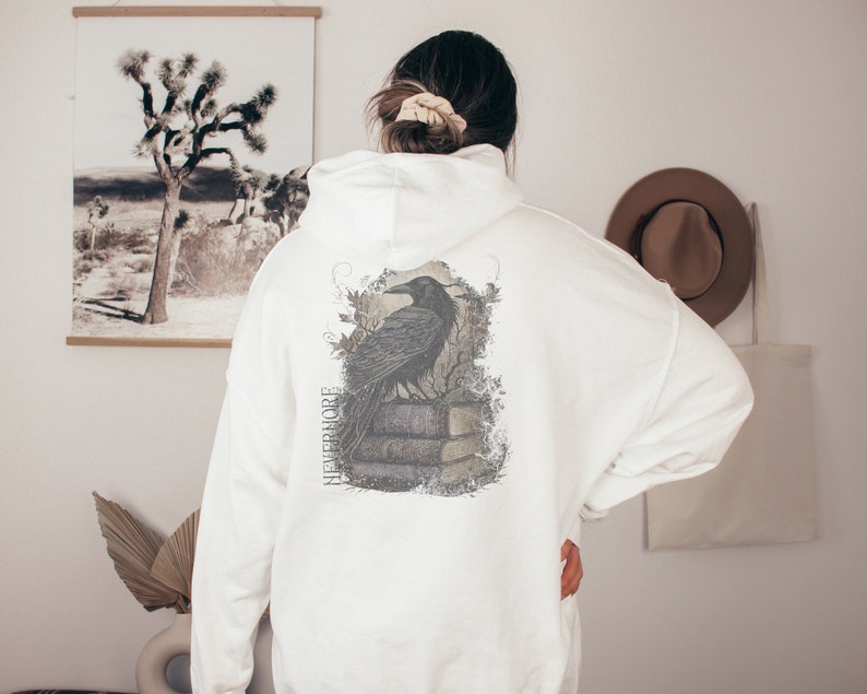 May include: White hooded sweatshirt with a black raven graphic on the back. The graphic features a raven perched on a stack of books with the word "Nevermore" printed vertically on the left side of the graphic.