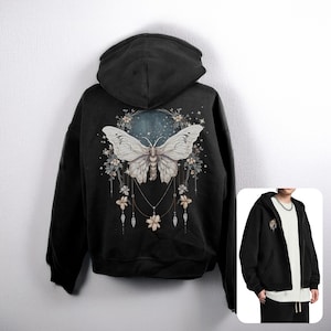 May include: Black zip-up hoodie featuring a large, detailed butterfly design on the back. The butterfly is white with intricate wing patterns, surrounded by floral and celestial elements. The hoodie has a hood and a front zipper.