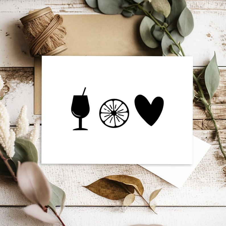 Puede incluir: Una tarjeta blanca con ilustraciones negras de una copa de vino, una rodaja de naranja y un coraz&oacute;n. La tarjeta est&aacute; sobre una superficie de madera con vegetaci&oacute;n y cuerda.