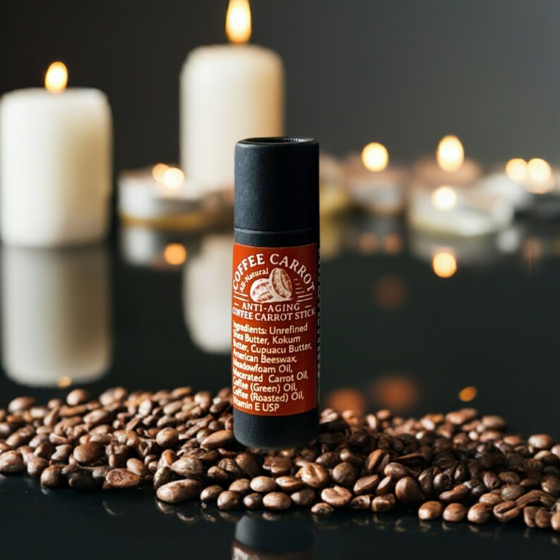 Puede incluir: Un tubo negro y rojo de "Coffee Carrot Anti-Aging Coffee Carrot Stick" descansa sobre granos de caf&eacute;. La etiqueta muestra los ingredientes. Velas encendidas en el fondo crean un ambiente c&aacute;lido. Producto para el cuidado de la piel.