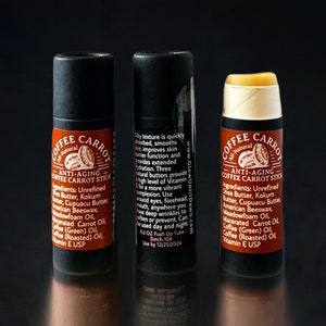 Puede incluir: Tres b&aacute;lsamos labiales Coffee Carrot Stick antiedad. Los tubos negros tienen una etiqueta marr&oacute;n con el nombre del producto y los ingredientes. El b&aacute;lsamo abierto es de color amarillo claro. El texto de la etiqueta incluye los ingredientes y las instrucciones de uso.