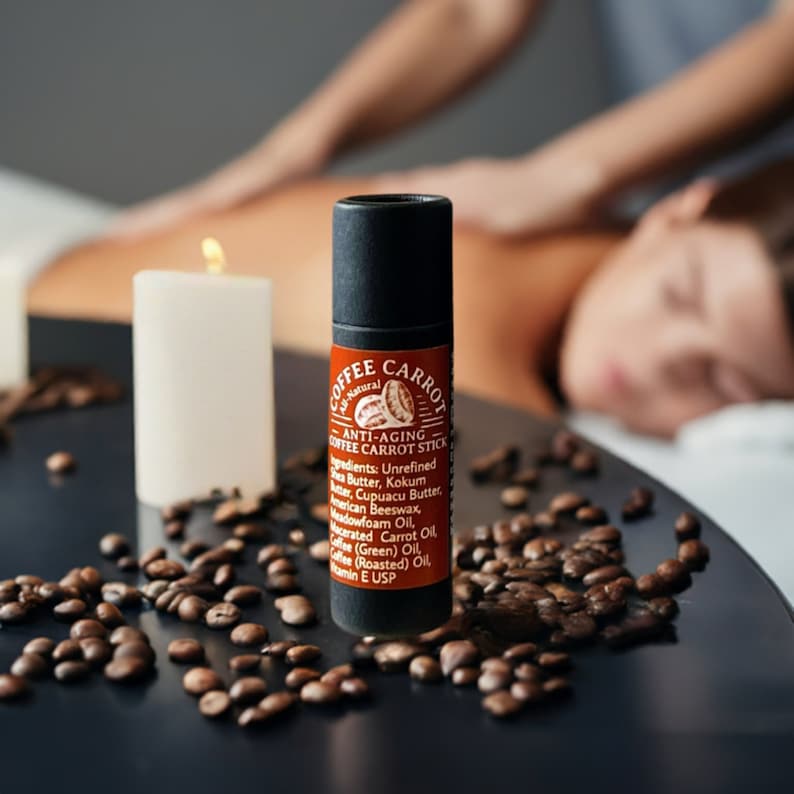 Puede incluir: Un stick anti-edad de caf&eacute; y zanahoria negro y marr&oacute;n con una etiqueta que enumera ingredientes como manteca de karit&eacute; y aceite de caf&eacute;. El stick est&aacute; rodeado de granos de caf&eacute; y una vela encendida. Una persona recibe un masaje en el fondo.