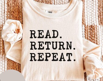 May include: An ivory long-sleeve shirt featuring the black text READ. RETURN. REPEAT. printed on the front. The garment has a crew neckline and a label at the inner collar. The fabric has a smooth texture and a solid light-colored appearance.