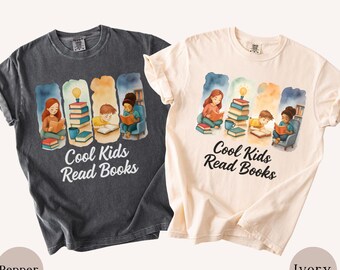 May include: Two short-sleeve crew neck t-shirts in pepper and ivory colors. Each shirt features a watercolor-style graphic of children reading books with a lightbulb icon and the text Cool Kids Read Books printed in a black script font below the art.