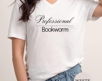 May include: A white short-sleeved t-shirt with a V-neckline featuring the black printed text Professional Bookworm centered on the chest. The shirt is paired with light blue drawstring bottoms, and a circular white label displays the word WHITE.