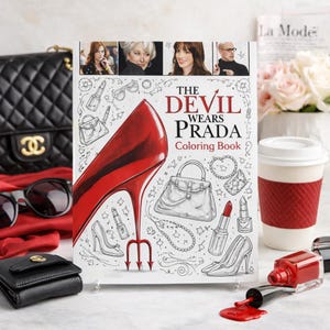 May include: A "The Devil Wears Prada" coloring book with a red high heel illustration. The book is surrounded by fashion accessories, including a black purse, sunglasses, and a coffee cup.