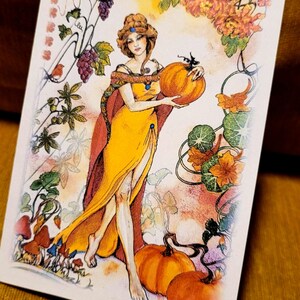 Könnte beinhalten: Eine Illustration im Vintage-Stil zeigt eine Frau in einem gelben Kleid, die einen großen orangefarbenen Kürbis hält. Das Kunstwerk zeigt Herbstlaub, Trauben und Kürbisse mit einer warmen Farbpalette aus Orange, Gelb und Rot.