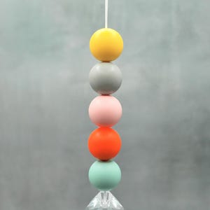 May include: A hanging decorative mobile featuring a string of colorful spheres in yellow, gray, pink, orange, and mint green, topped with a clear crystal prism. The spheres are evenly spaced.