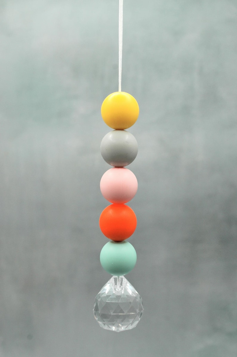 May include: A hanging decorative mobile featuring a string of colorful spheres in yellow, gray, pink, orange, and mint green, topped with a clear crystal prism. The spheres are evenly spaced.